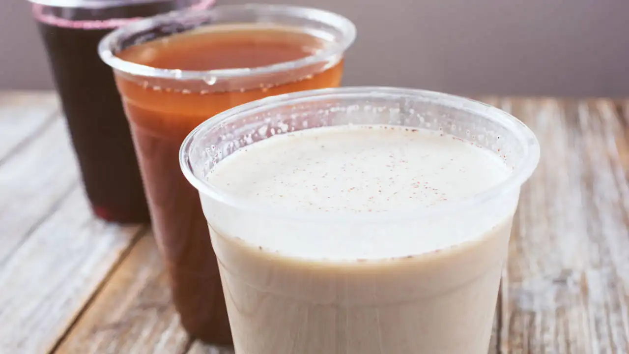 Tres vasos de plástico llenos de bebidas tradicionales ecuatorianas sobre una mesa de madera.