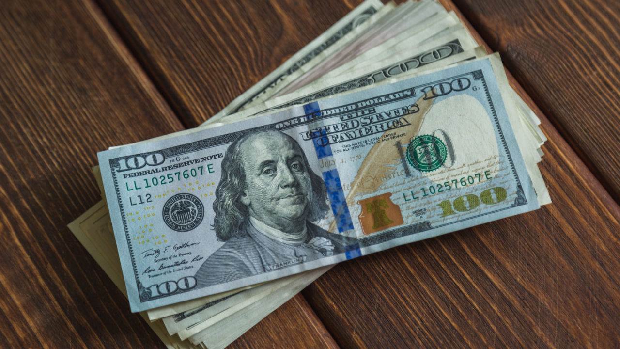 Una pila de billetes de 100 d&oacute;lares sobre una mesa de madera.