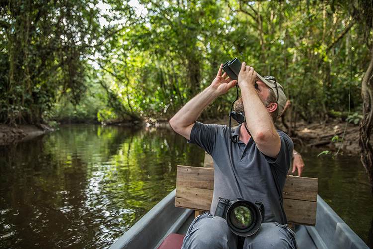 Un hombre en una canoa mirando a través de binoculares.