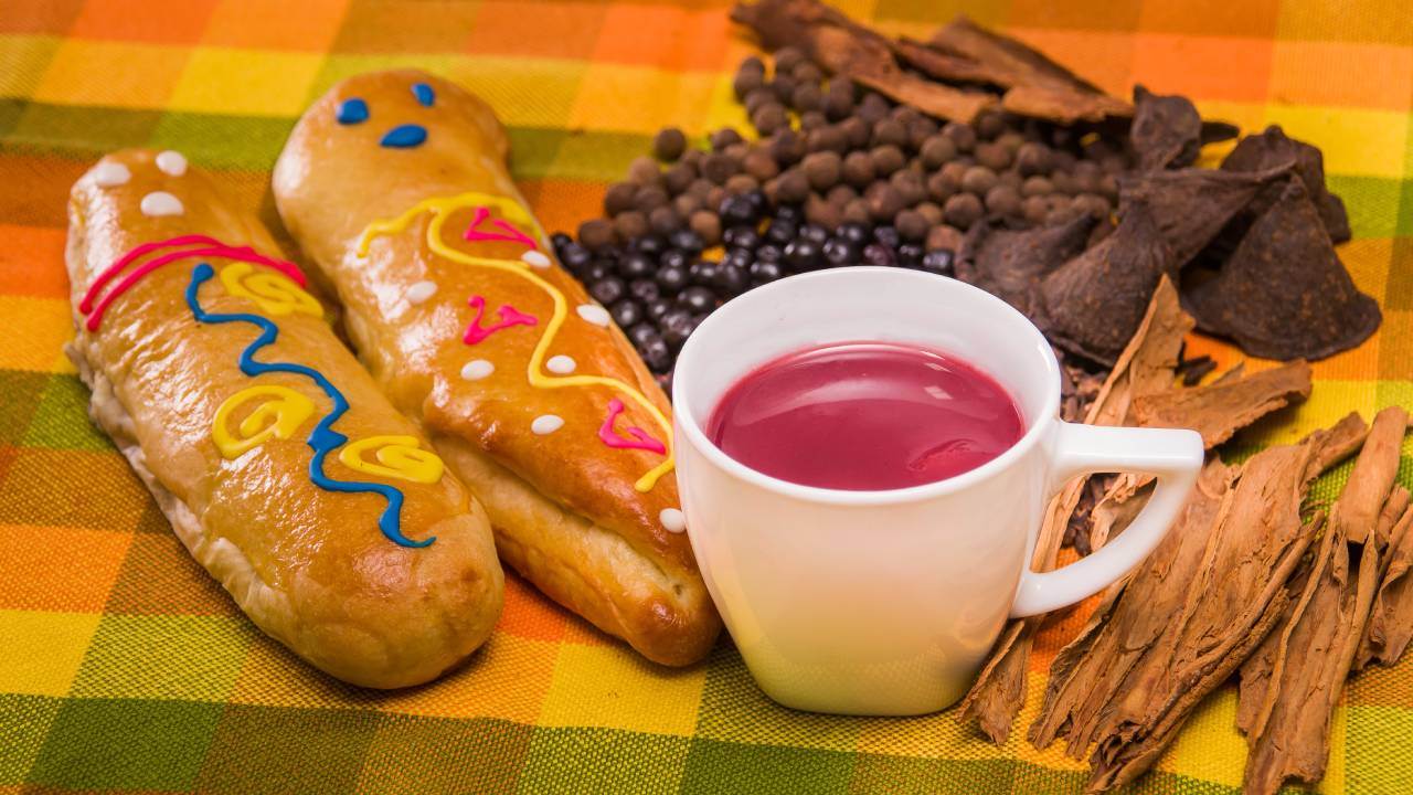 Una taza de té rojo, pan decorado y especias sobre un colorido mantel a cuadros.