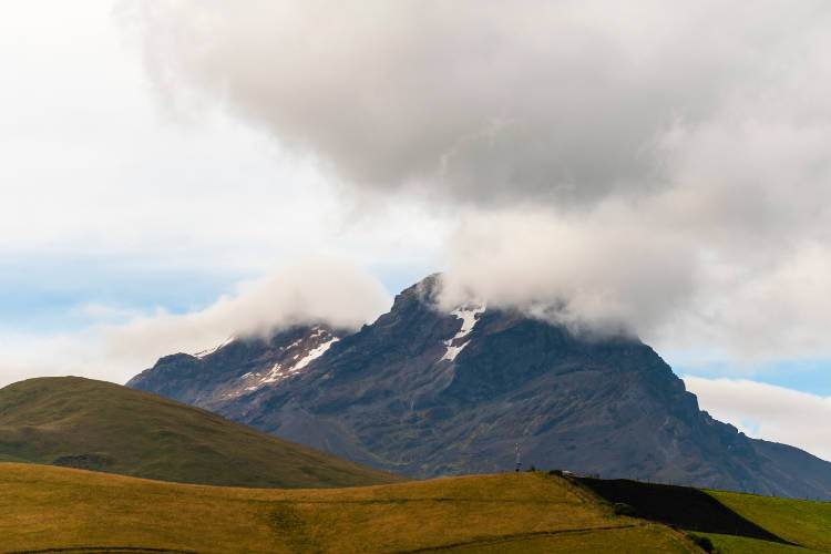 Una monta&ntilde;a cubierta de nubes con un campo de hierba al fondo.