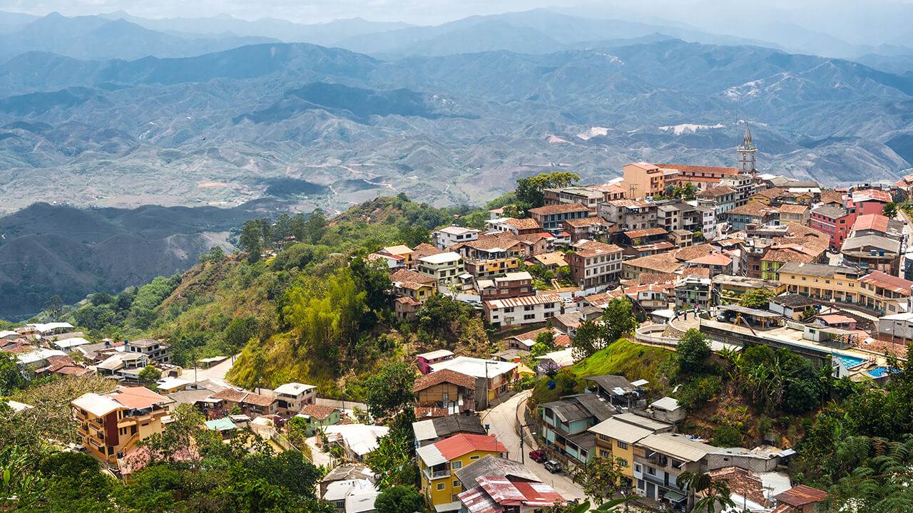 Una vista panorámica de un pueblo en la ladera de una colina con casas densamente pobladas y una iglesia, con vistas a un paisaje montañoso.